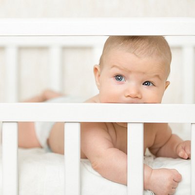 Cute baby in a cot sucking the wooden board