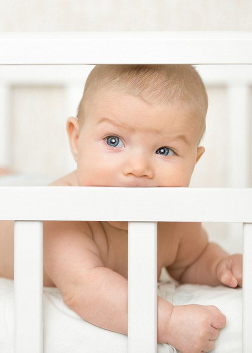 Cute baby in a cot sucking the wooden board