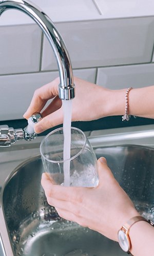 Woman filling the glass with water from the steel faucet in the kitchen