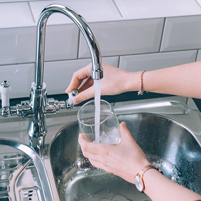 Woman filling the glass with water from the steel faucet in the kitchen