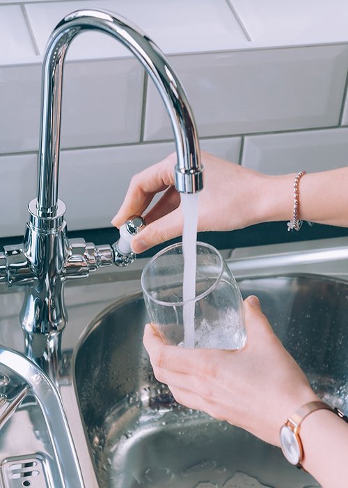 Woman filling the glass with water from the steel faucet in the kitchen