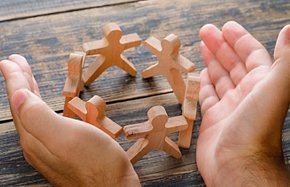 Business success concept on wooden background high angle view. hands protecting wooden figures of people.