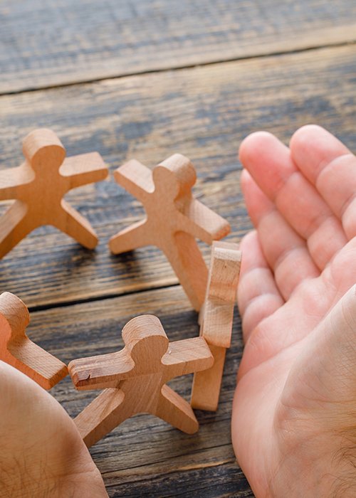 Business success concept on wooden background high angle view. hands protecting wooden figures of people.